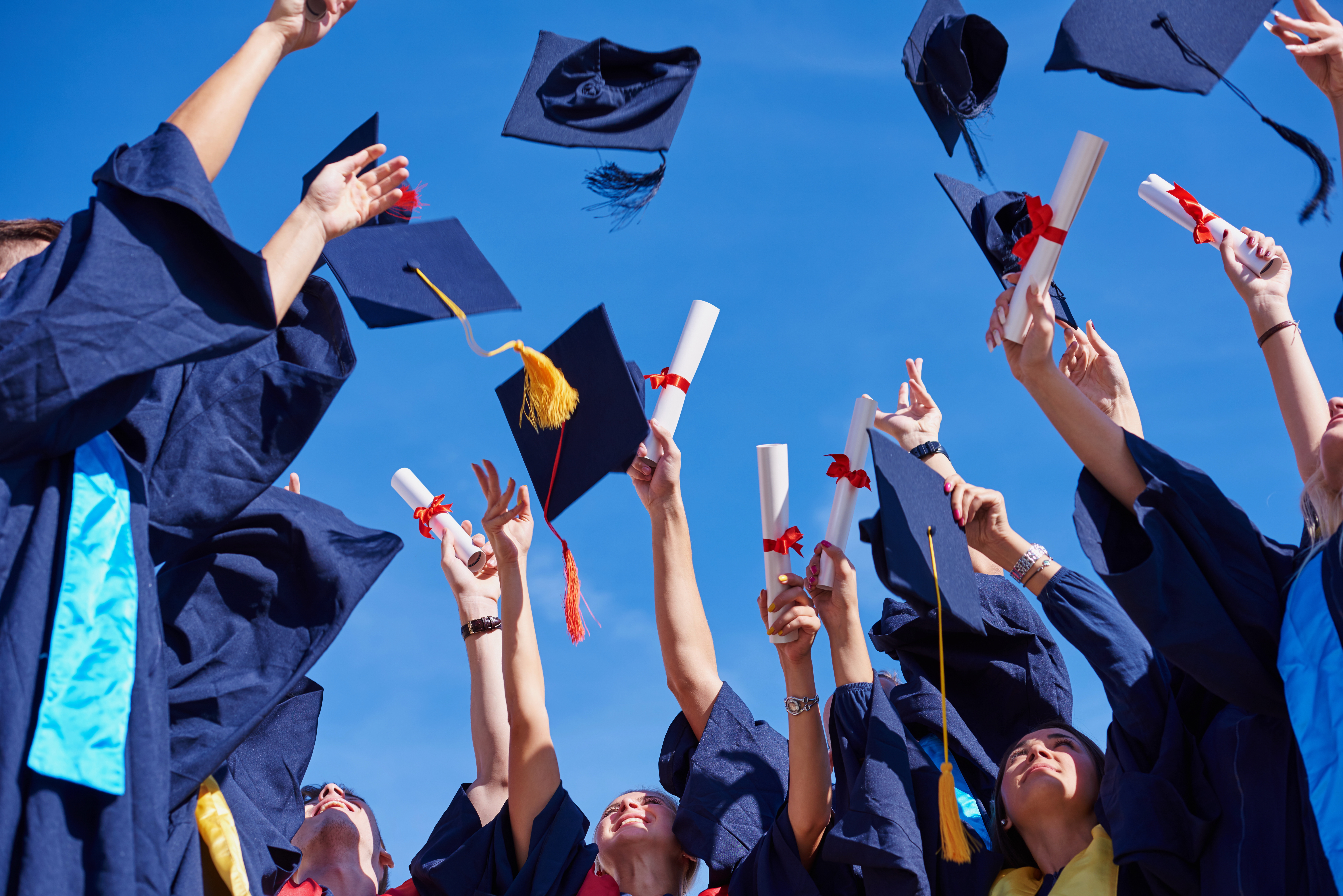 college students graduates tossing up hats over blue sky.
